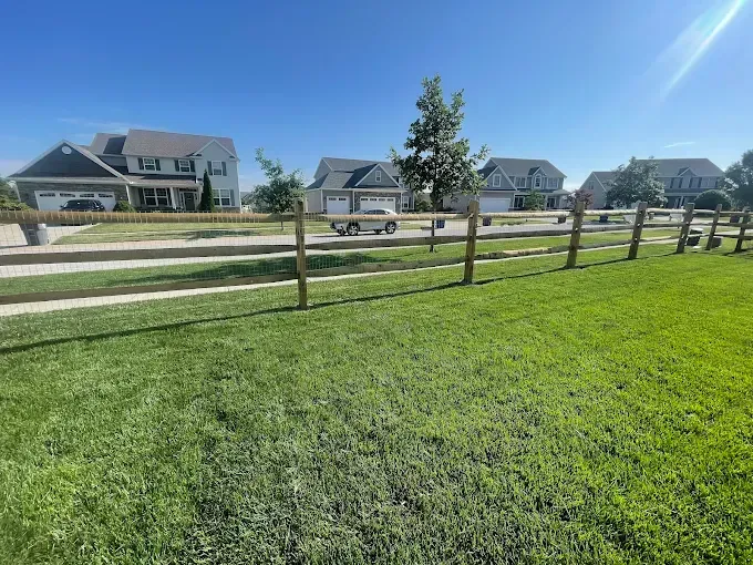 Green lawn, wooden fence, suburban homes under blue sky.