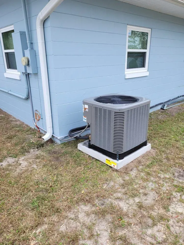 Air conditioning unit on a concrete pad next to a light blue house.