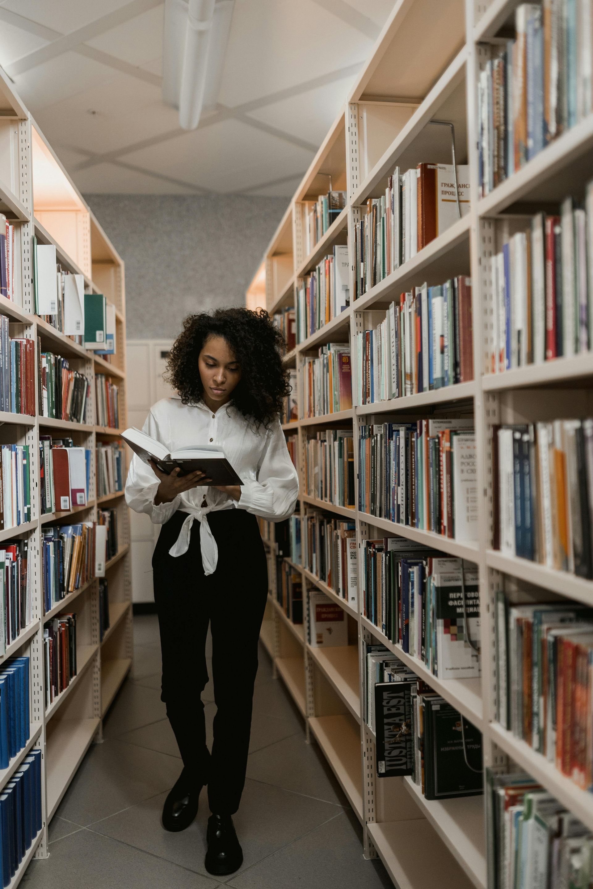 a girl reading a book in between two wooden shelves