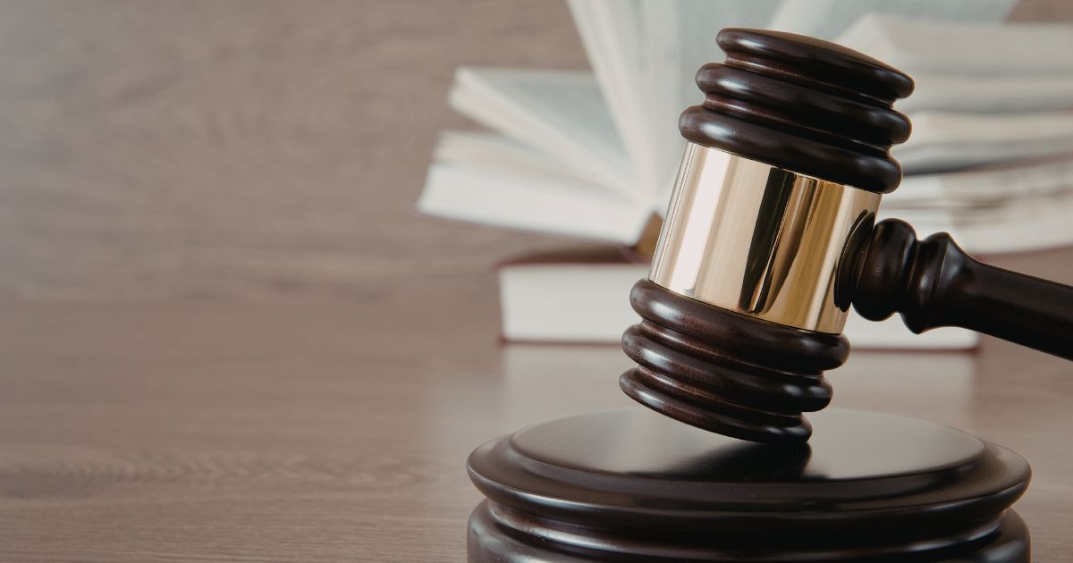 A dark wooden gavel resting on a sound block with an open book blurred in the background.