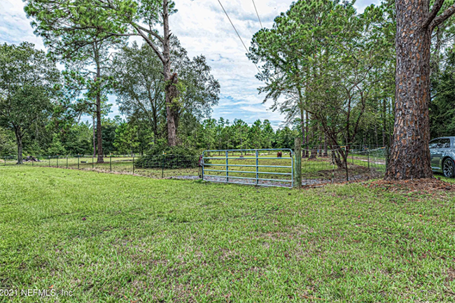 Grassy field with gate, trees, and cloudy sky in the background.