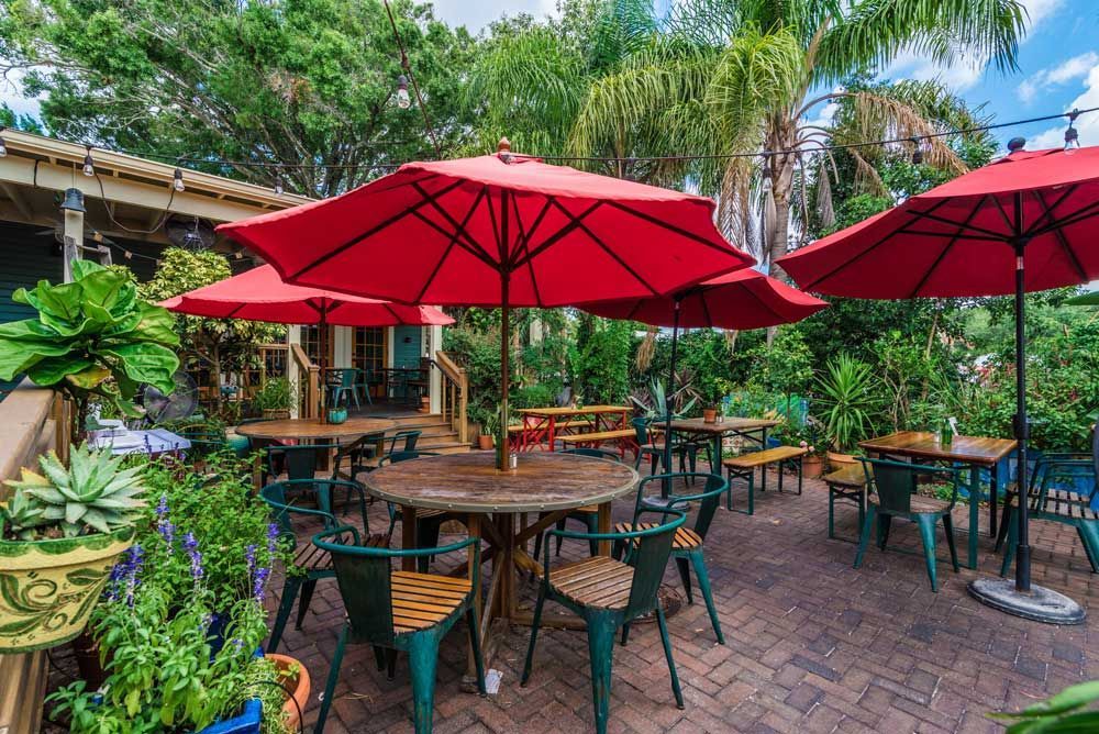 Outdoor cafe with red umbrellas, tables, chairs, and lush greenery.