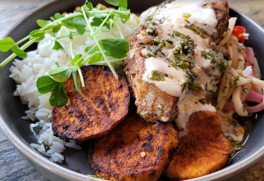 Bowl with rice, sweet potatoes, and chicken topped with sauce and greens.