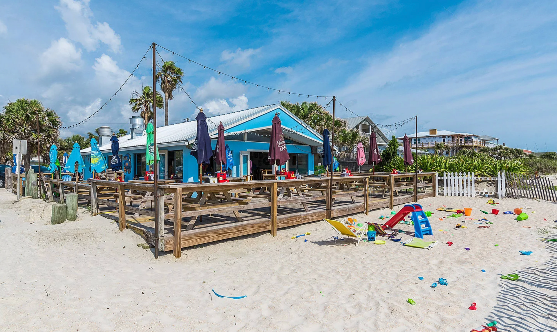 Beachside restaurant with blue exterior and wooden deck, playground in front.