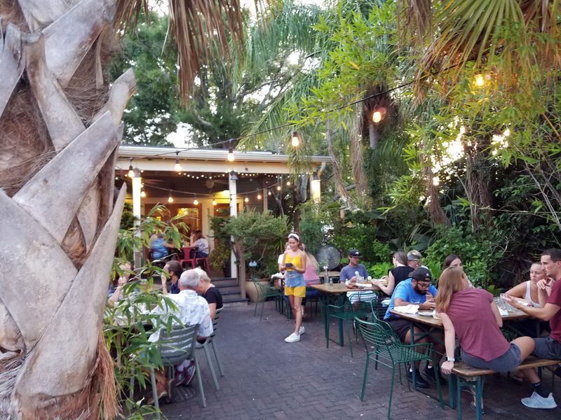 Outdoor restaurant patio with patrons at tables under string lights and trees.