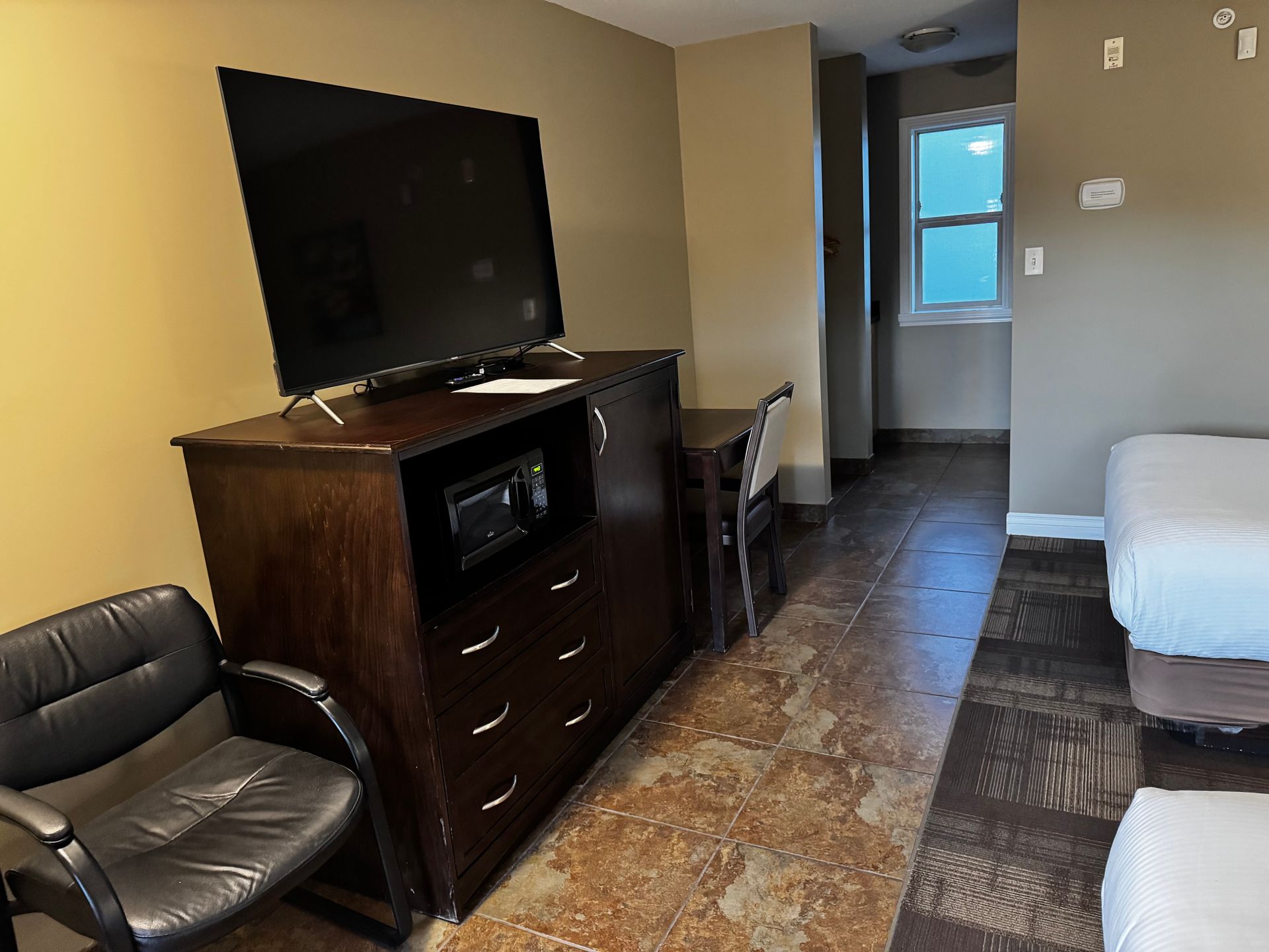 Hotel room with TV, dresser, chair, desk, beds, and bathroom doorway.