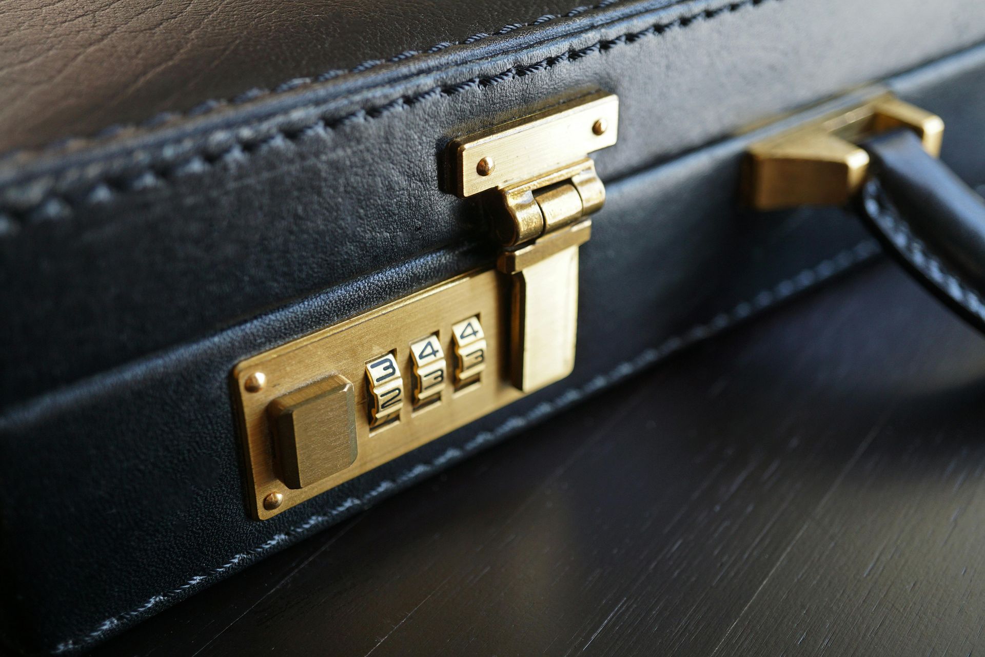 Close-up of a black briefcase with a gold combination lock on a dark surface.