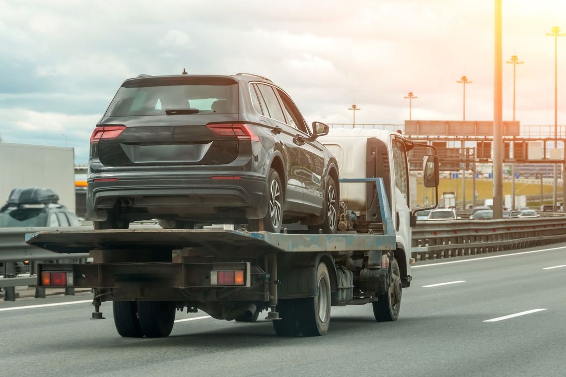 Black SUV on a tow truck driving on a highway at sunset