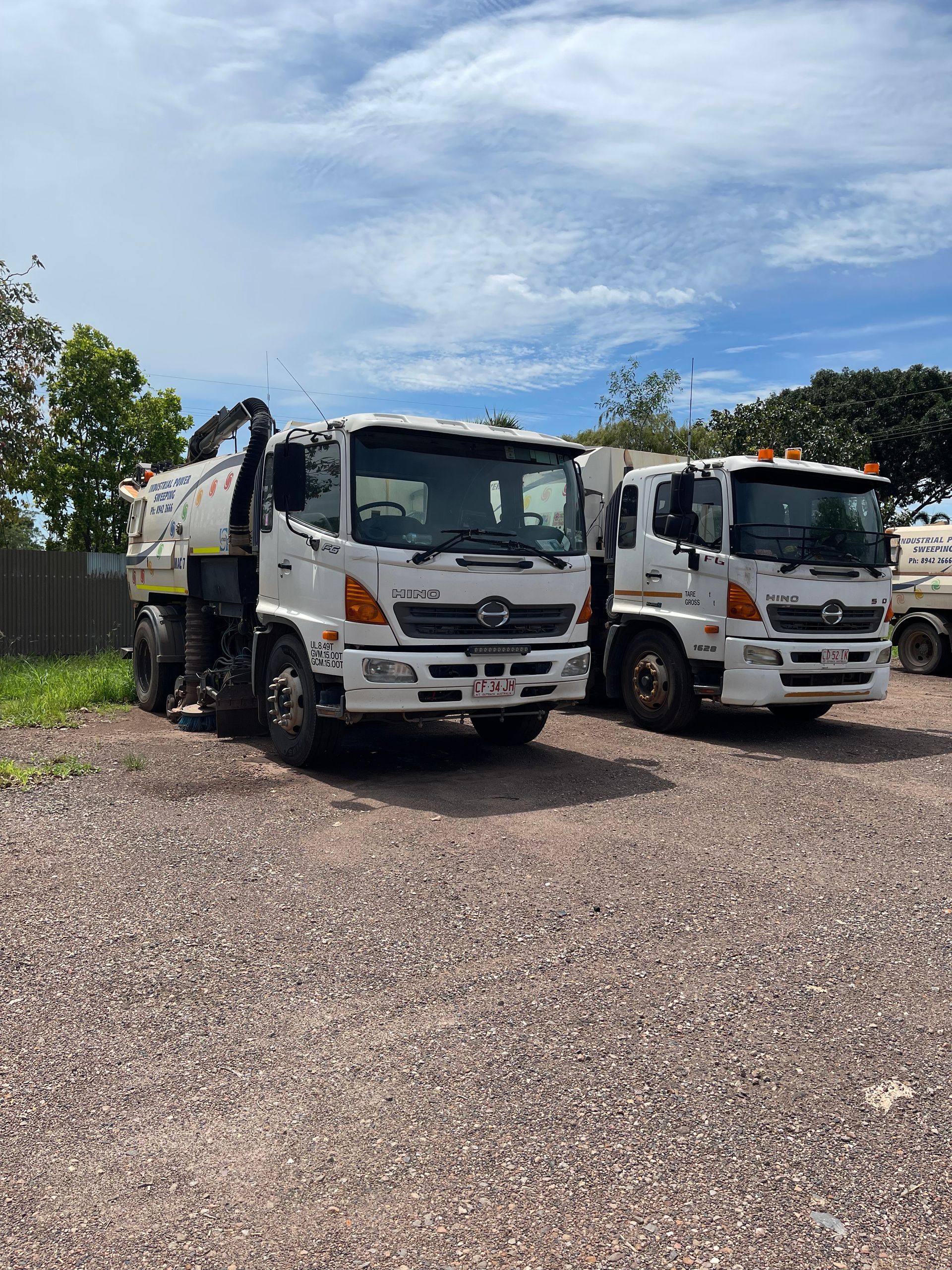 Two white trucks parked on gravel under a partly cloudy sky  — Industrial Power Sweeping Services Pty Ltd In Knuckey Lagoon, NT