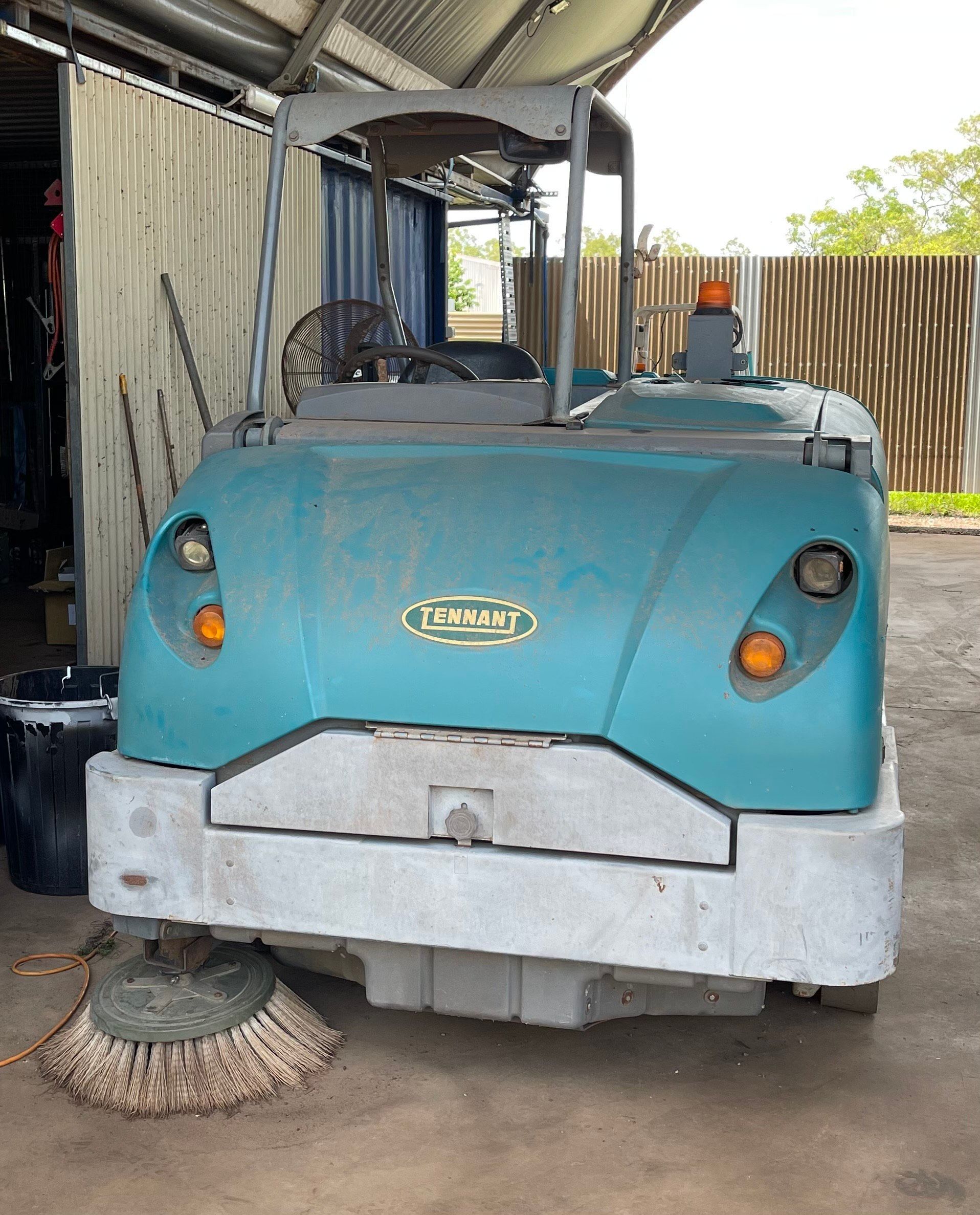 Turquoise industrial sweeper with a driver's seat, brushes, and an orange light, inside a garage — Industrial Power Sweeping Services Pty Ltd In Knuckey Lagoon, NT