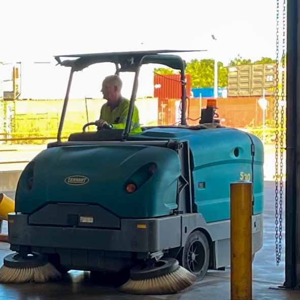 A teal industrial sweeper with a driver, cleaning a warehouse floor near cargo containers  — Industrial Power Sweeping Services Pty Ltd In Knuckey Lagoon, NT