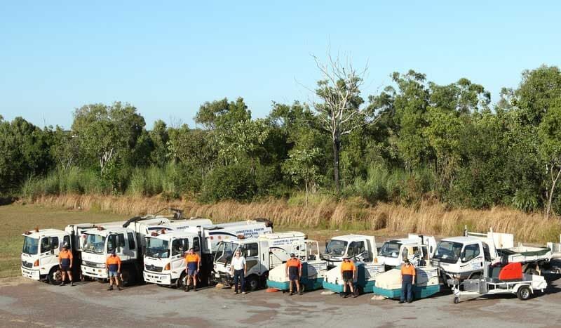 A group of white utility vehicles parked in front of a treeline, with people in workwear standing near them — Industrial Power Sweeping Services Pty Ltd In Knuckey Lagoon, NT