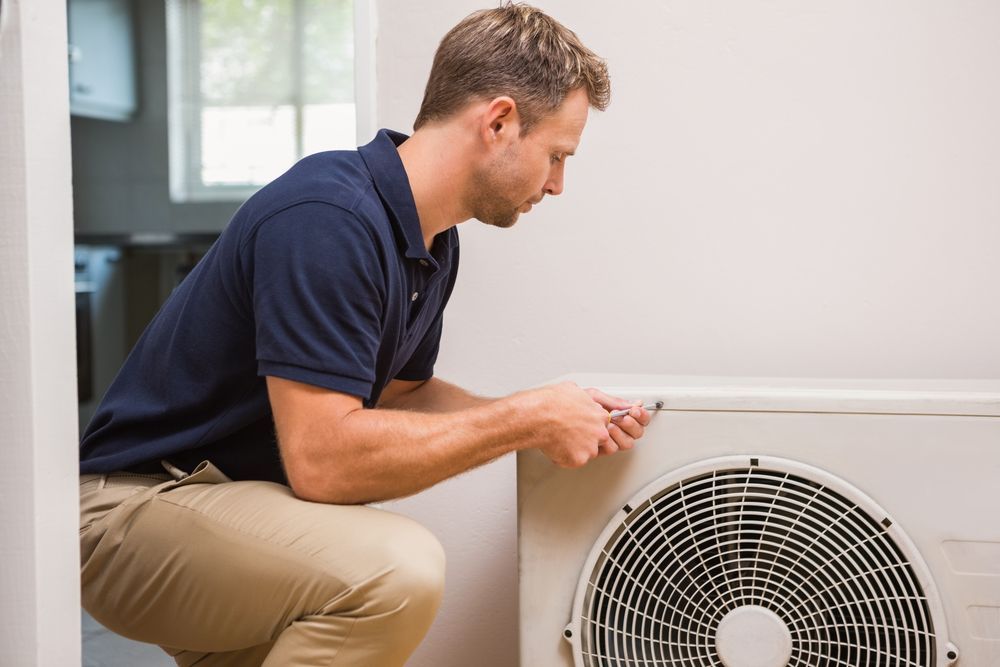 A Man Is Kneeling Down To Fix An Air Conditioner — Law Air Conditioning In Townsville, QLD