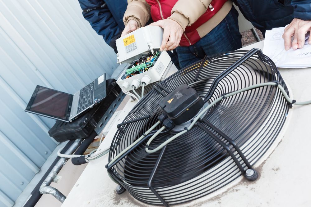 Two People Are Working On A Large Fan On A Table — Law Air Conditioning In Annandale, QLD