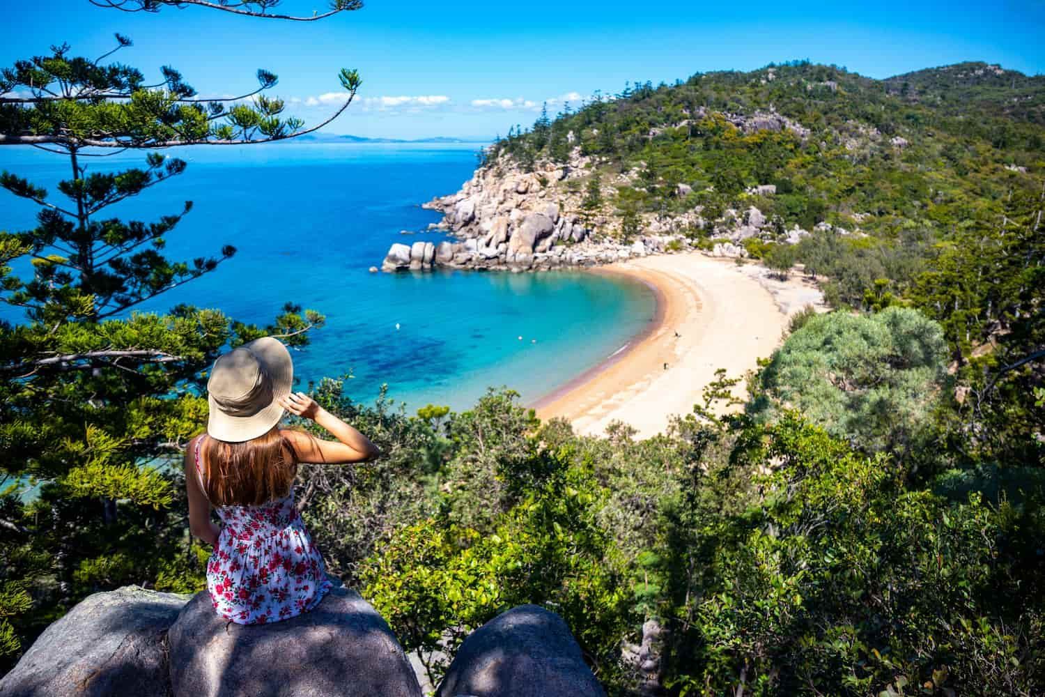 A Woman Is Sitting On A Rock Overlooking A Beach — Law Air Conditioning In Magnetic Island, QLD