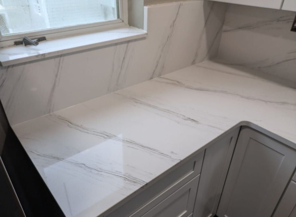 White marble-look countertop with gray veining beside a window and gray cabinets in a kitchen corner