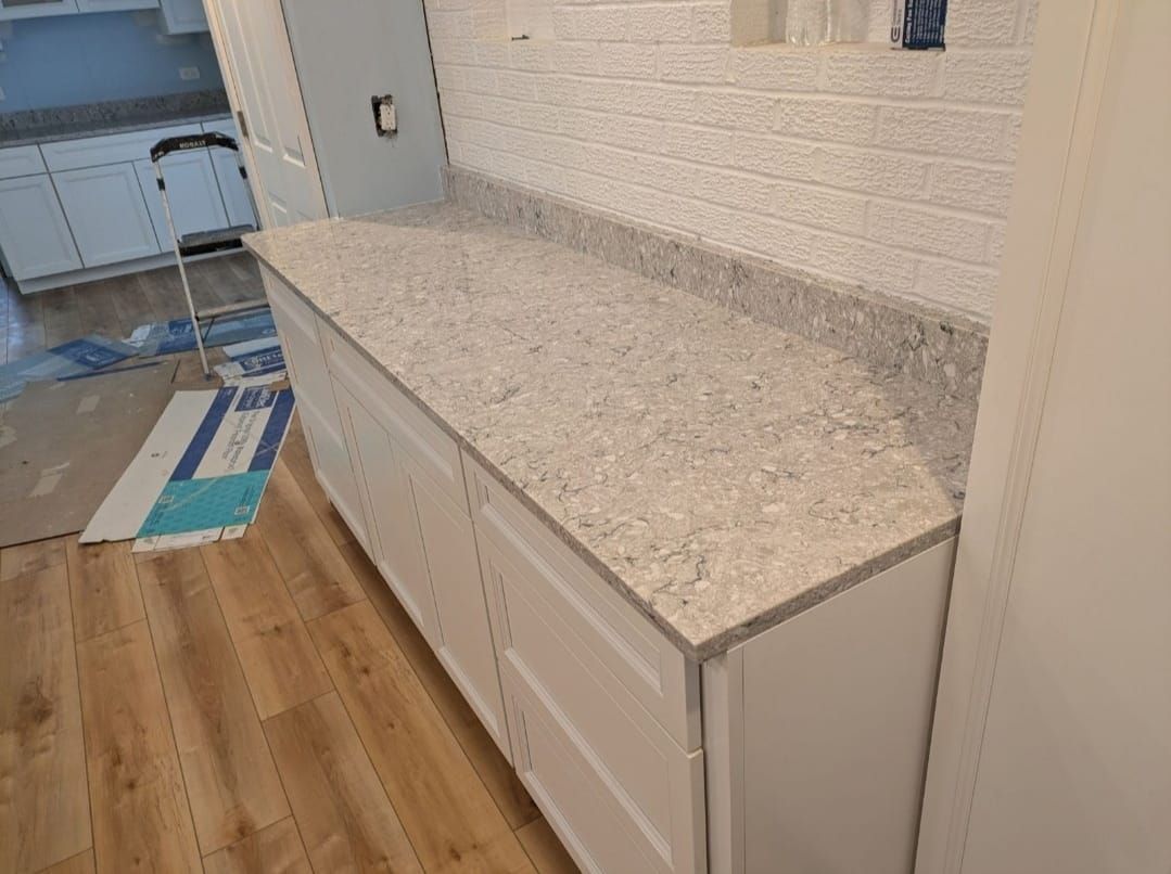 White quartz countertop over white cabinets in a kitchen under renovation, with a blue mat on the floor.