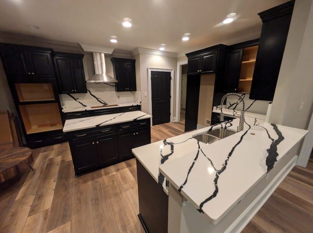 Modern kitchen with dark cabinets, white marble island, stainless appliances, and wood floors