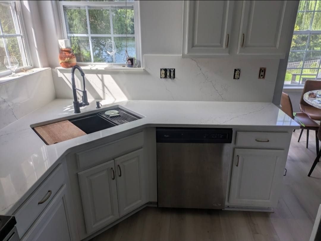 Modern kitchen with white countertops, gray cabinets, stainless dishwasher, and sunlight by the sink.