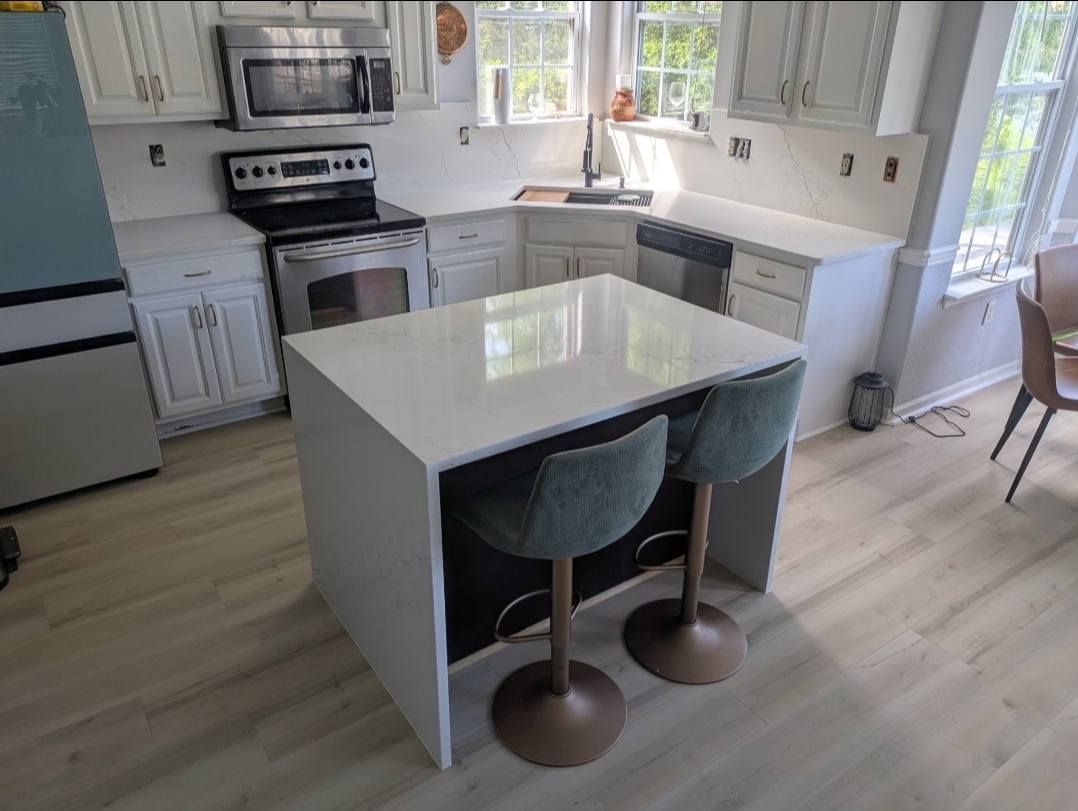 Bright kitchen with white cabinets, stainless appliances, and a marble island with two gray stools.