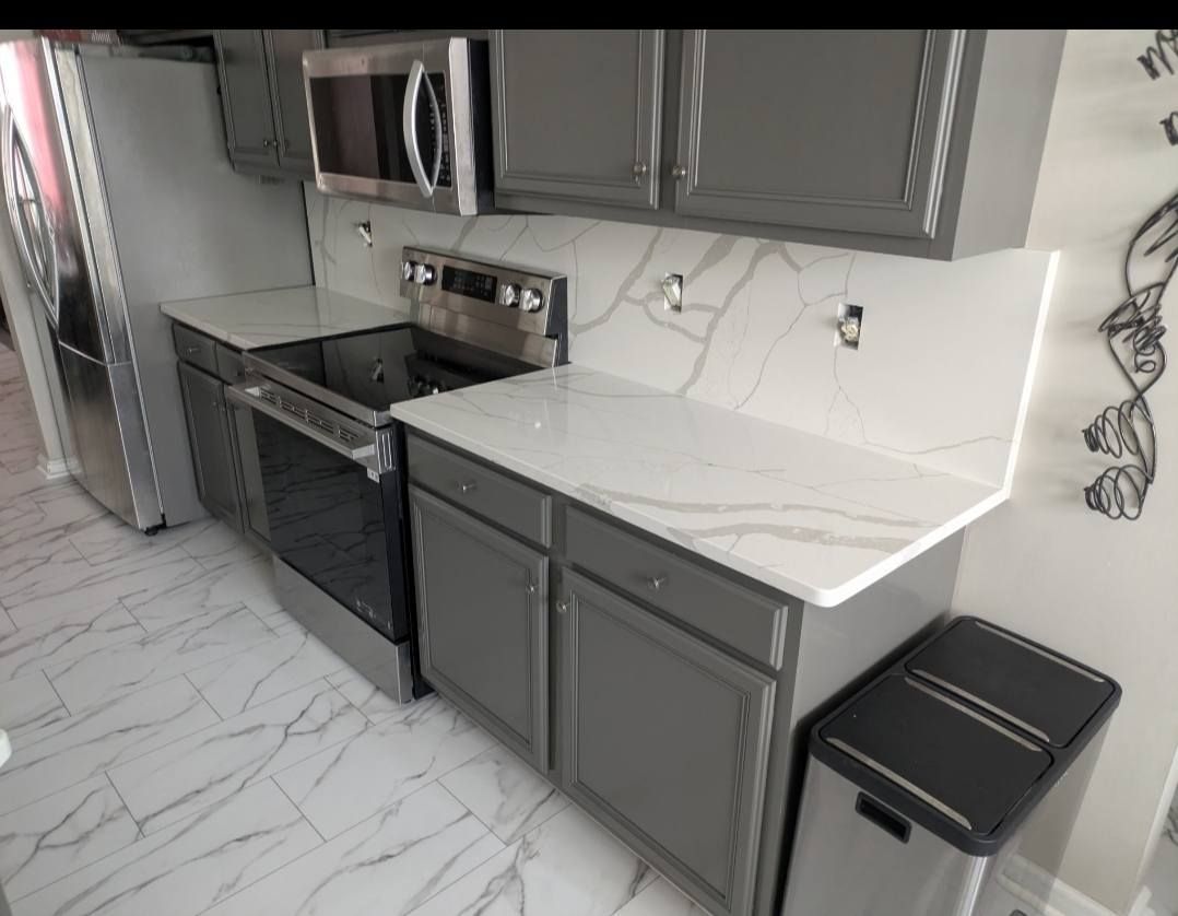 Modern kitchen with gray cabinets, white countertops, stainless appliances, and marble-look tile floor