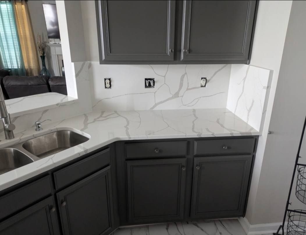 Modern kitchen with dark cabinets, marble-look backsplash, sink, and countertop.