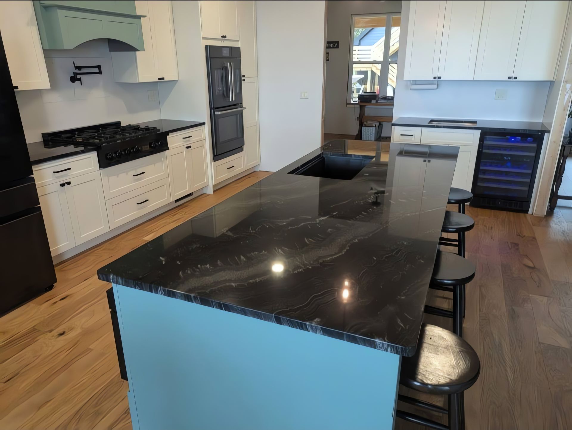 Bright modern white kitchen with large marble island, pendant lights, stainless fridge, and wooden sideboard.