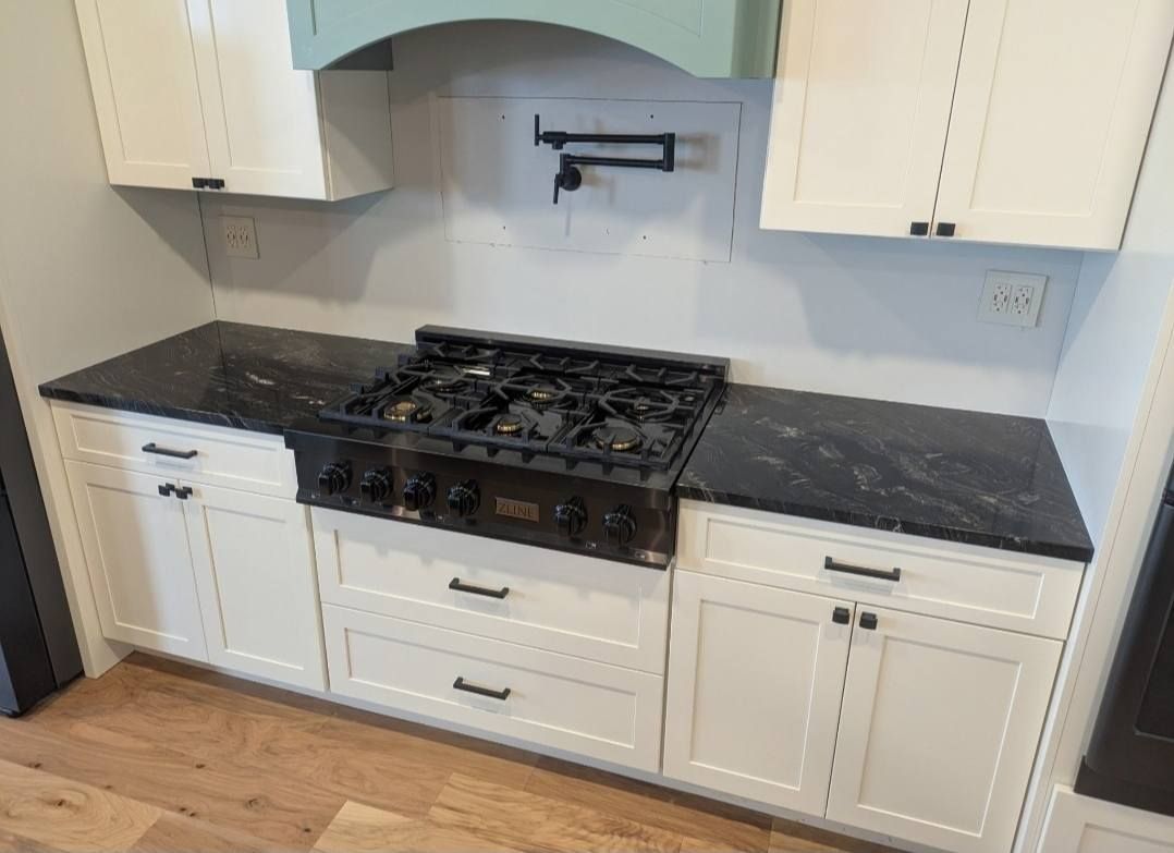 Kitchen with white cabinets, black countertops, and a black gas range beneath a mint-green backsplash.