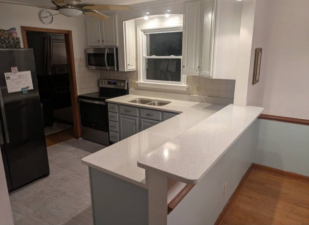 Kitchen with black appliances, white cabinets, and a long white breakfast bar.