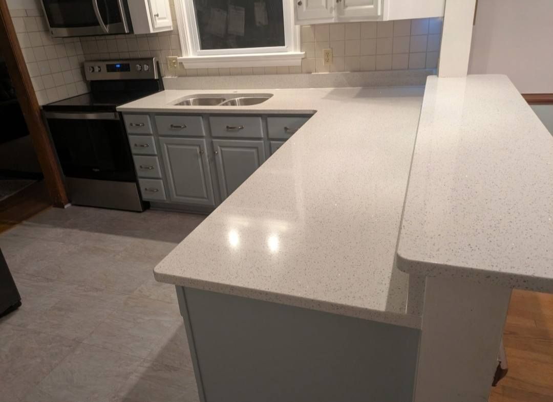 Modern kitchen with white countertops, gray cabinets, stainless oven, and sink by a window