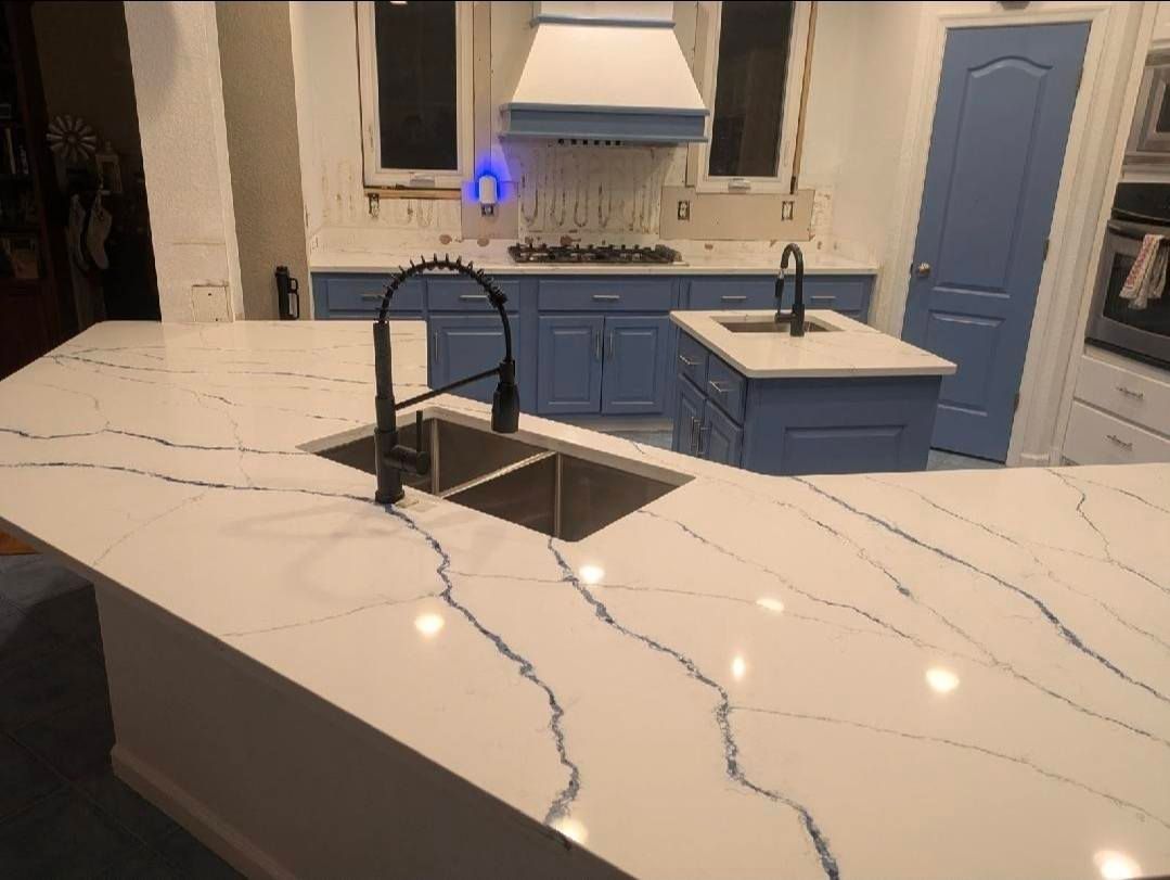 Modern kitchen with white marble island, black sink, blue cabinets, and stainless range hood