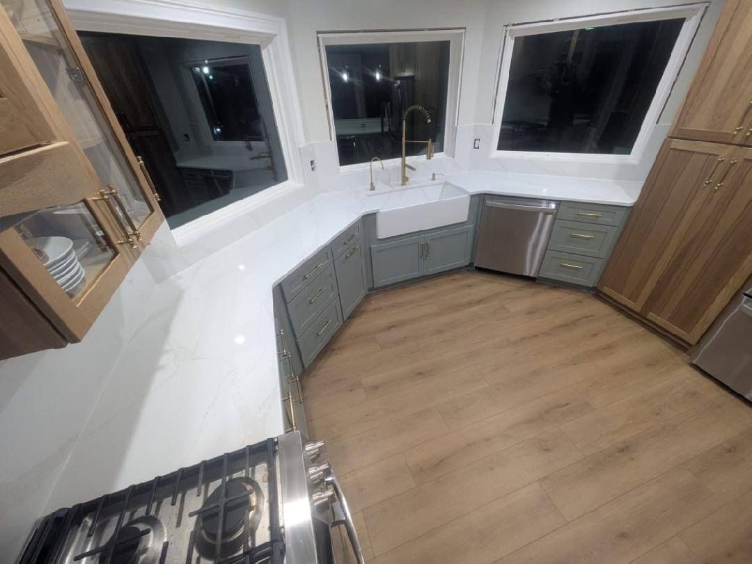 Modern kitchen with white countertops, gray cabinets, wood floor, and large windows at night