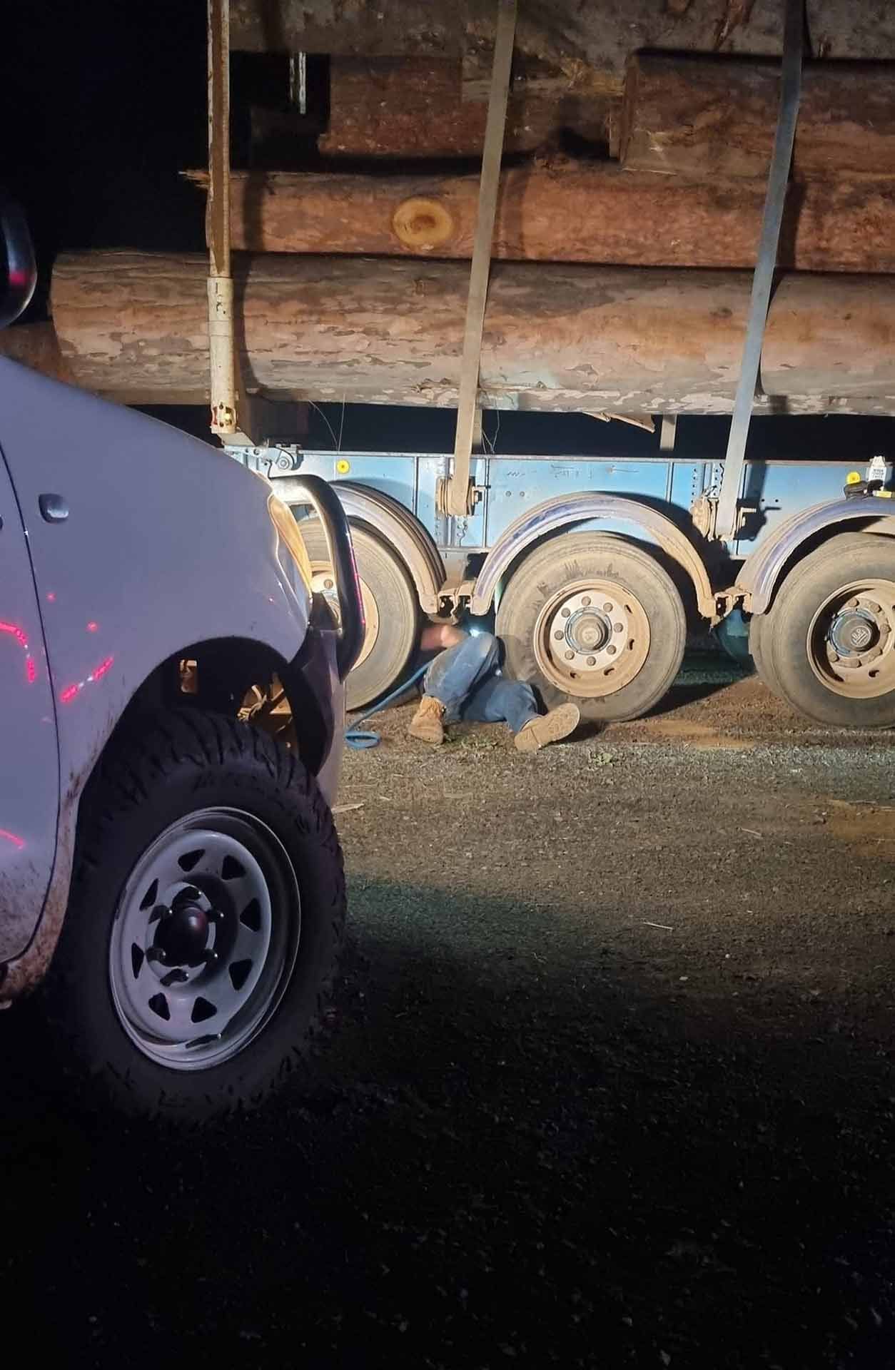 A Man Is Laying Under A Truck Carrying Logs — Mundubbera Tyre Service In Mundubbera, QLD