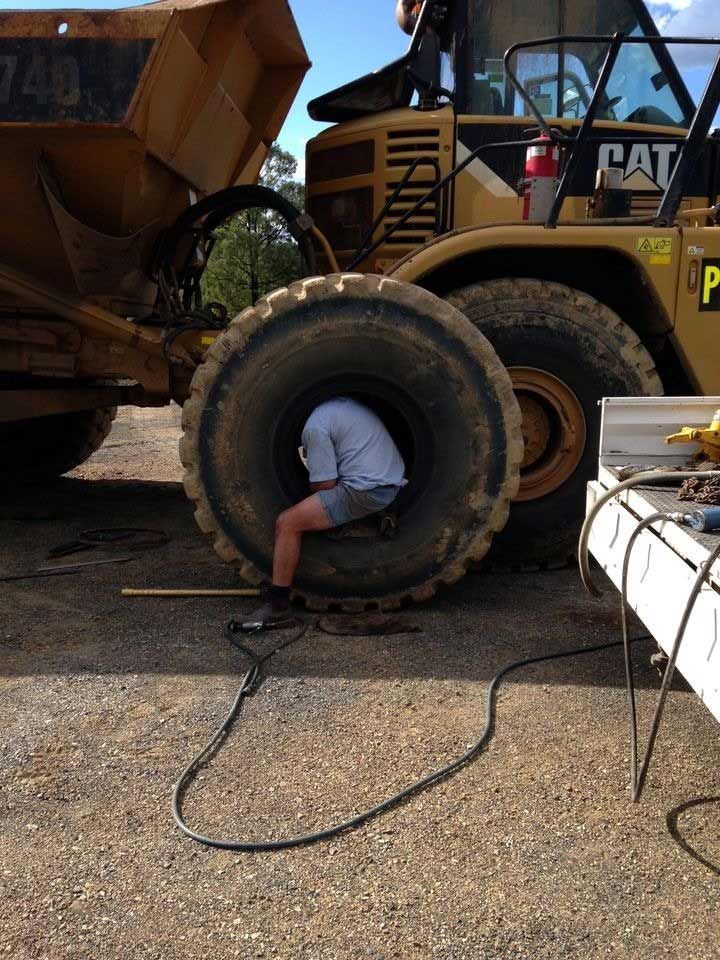 A Man Is Sitting In A Tire Next To A Cat Truck — Mundubbera Tyre Service In Mundubbera, QLD