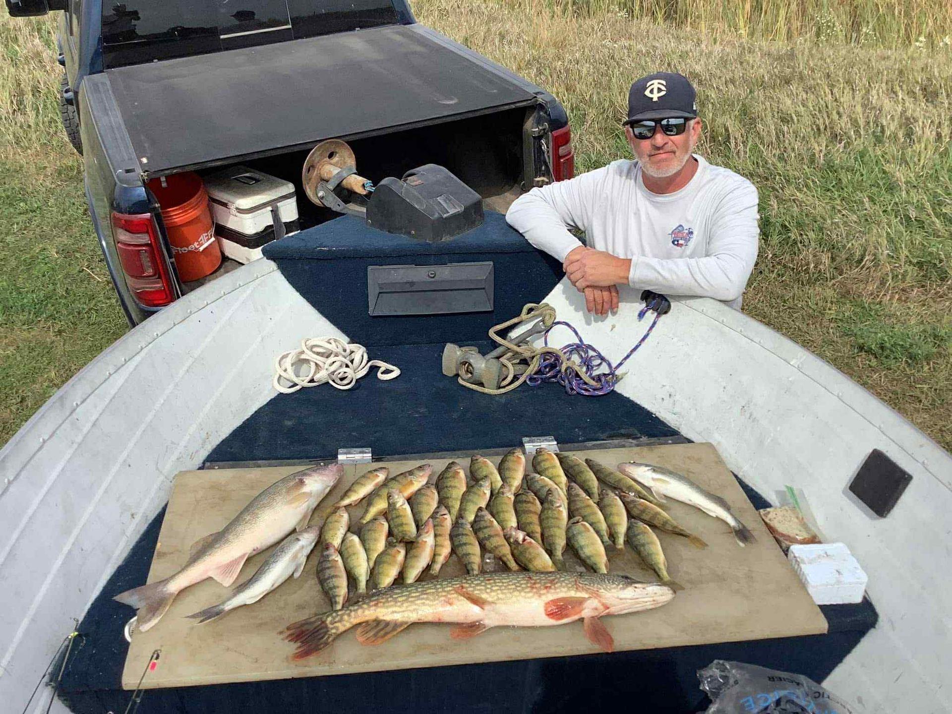 Man in boat displays caught fish. Dodge RAM in background.