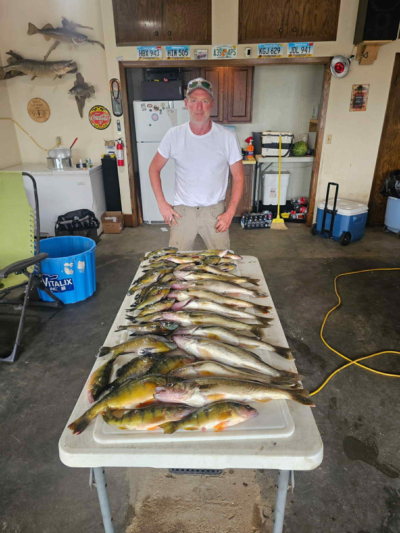 Man stands behind a table overflowing with freshly caught fish. Indoor setting.