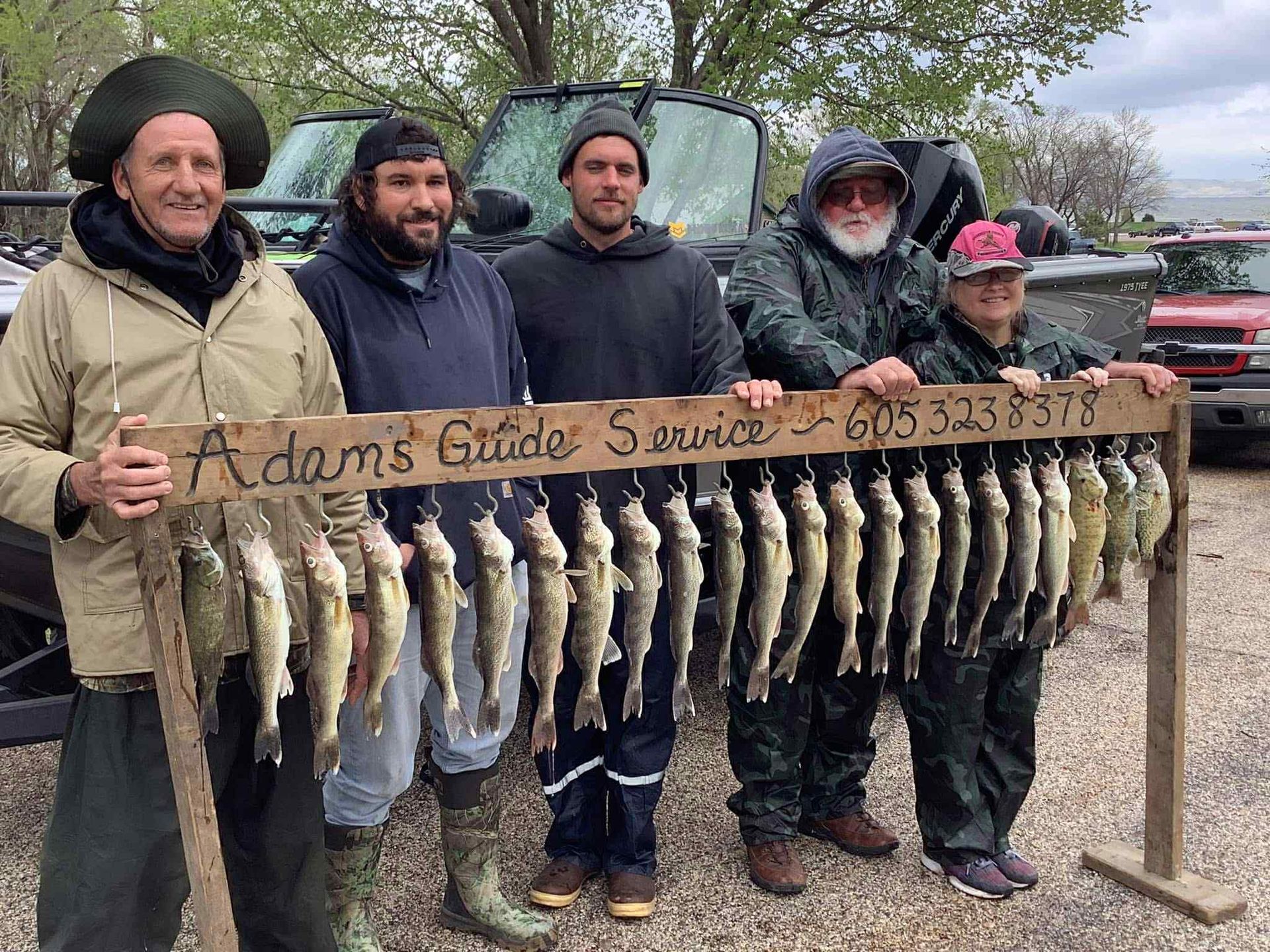 Five people with fish display, outdoors with vehicle. The sign says, 