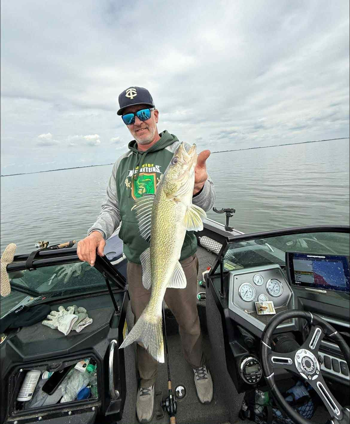 Man on boat holding a large walleye fish. Cloudy sky over the water.