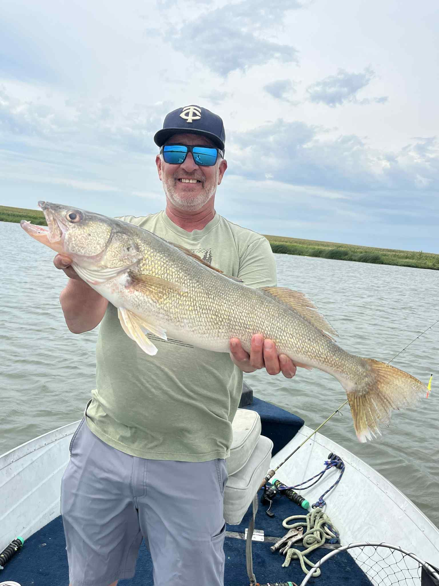 Man on boat holding large fish; marsh in background.