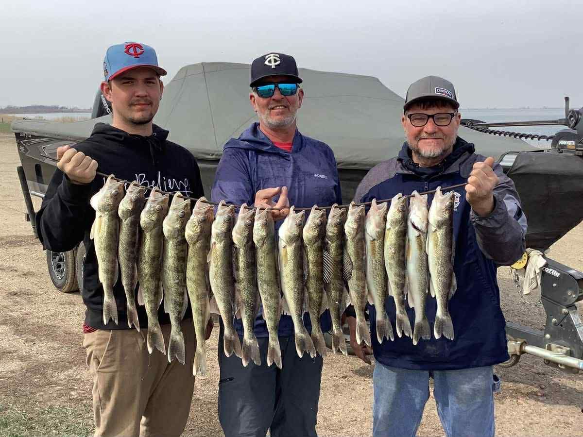 Three people holding a string of caught fish near a boat.