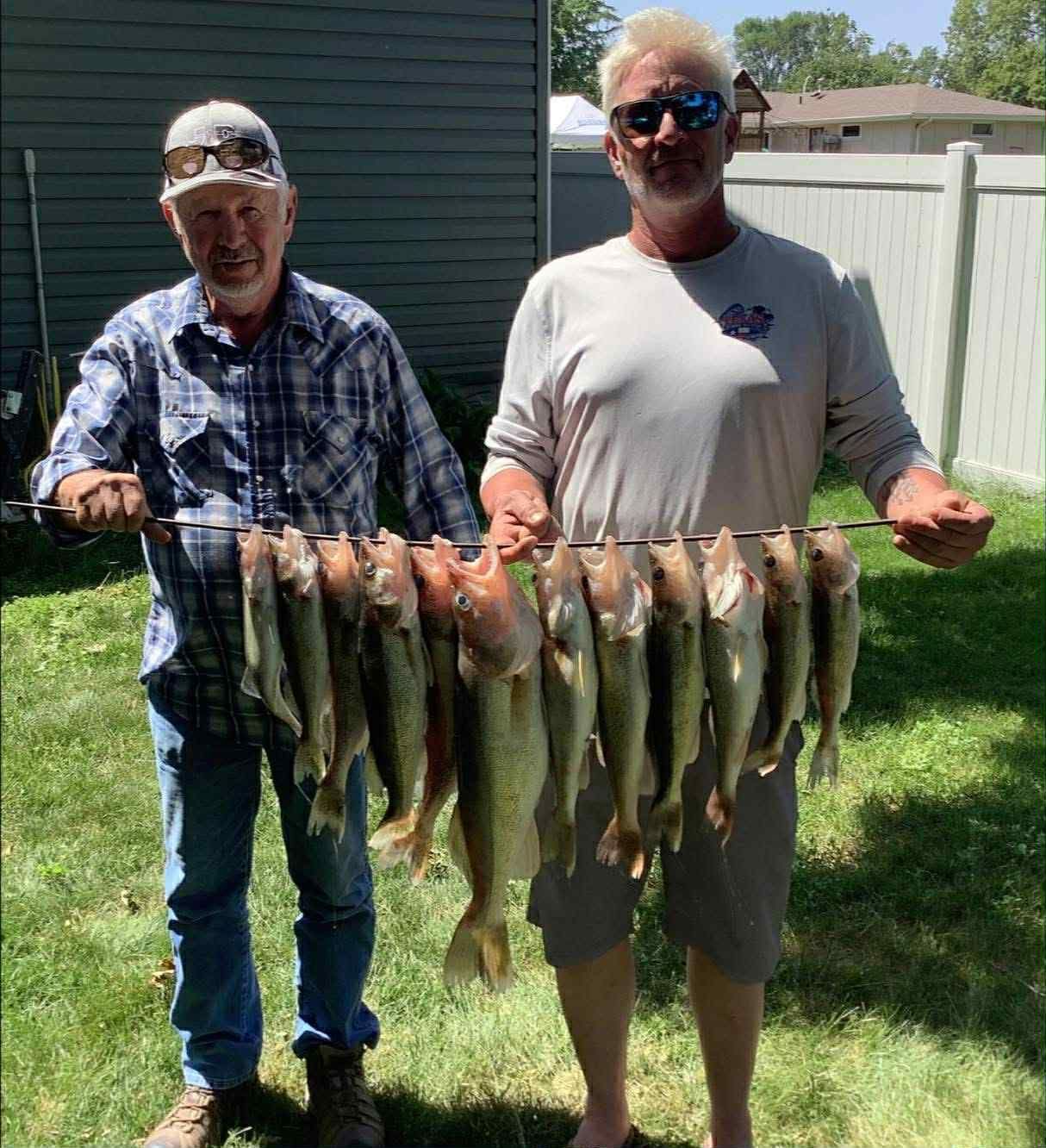 Two men holding a stringer with many caught fish in a grassy yard.