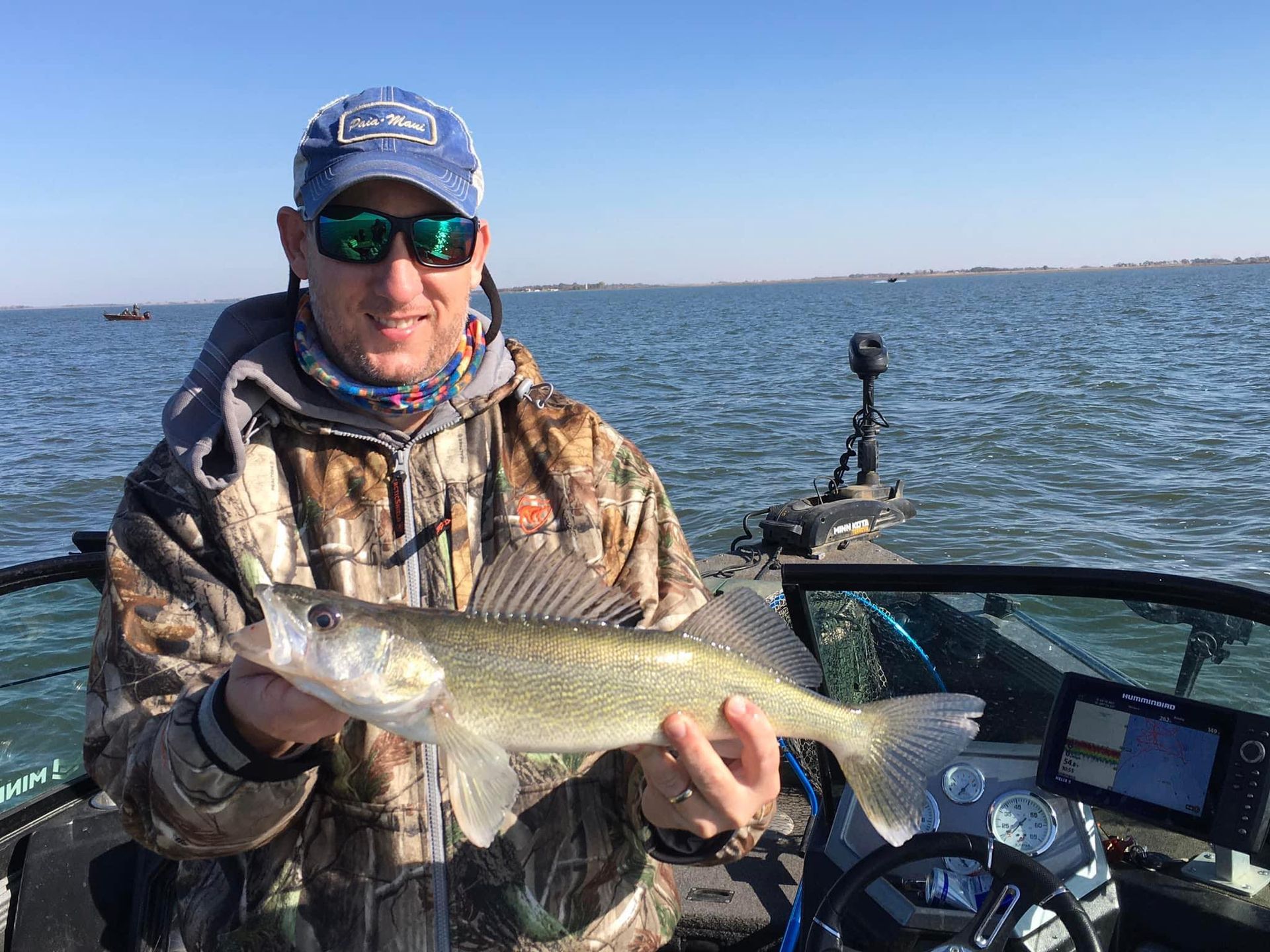Man in camo holding large fish in Lund boat on Lake Thompson