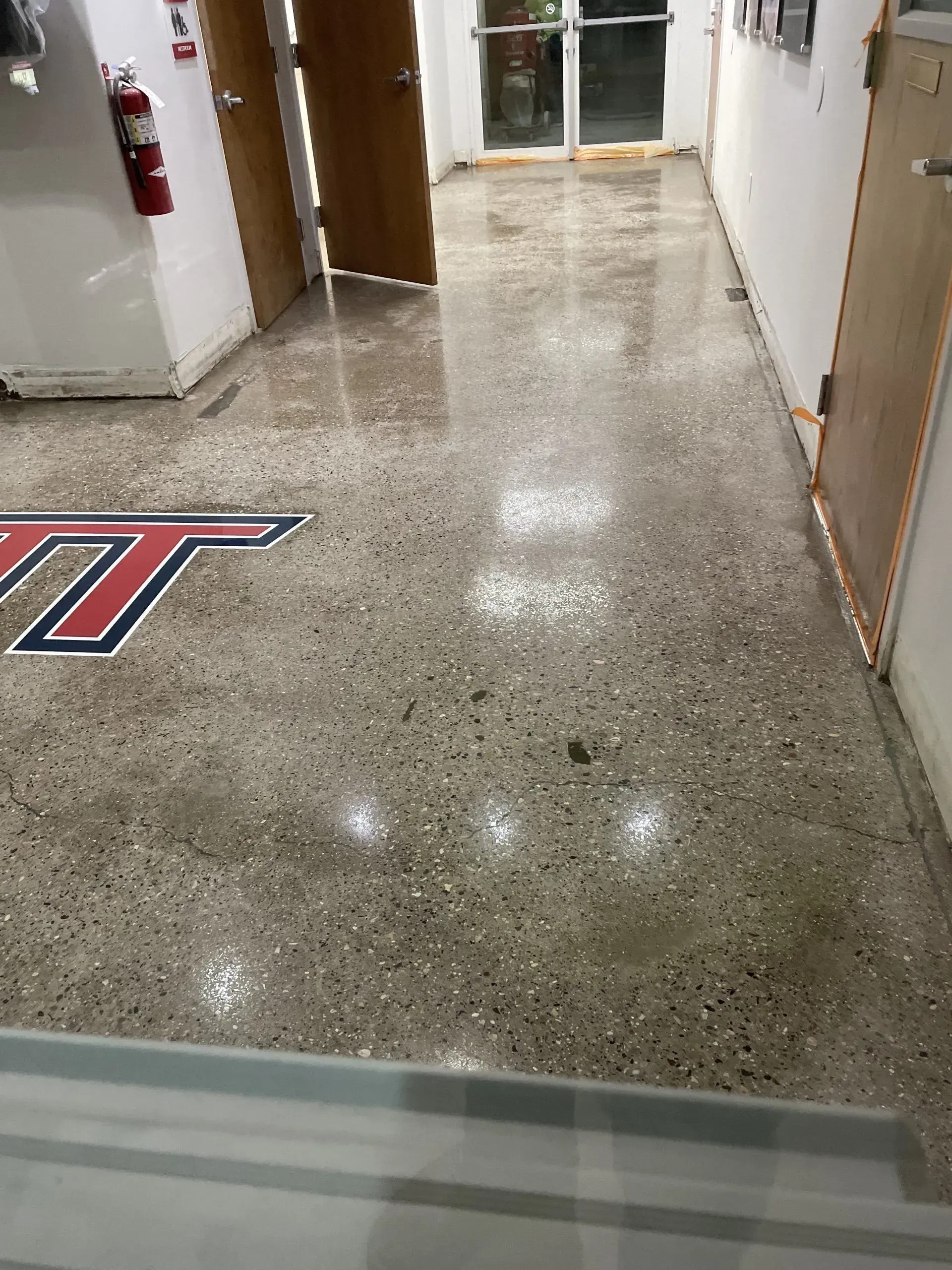 Polished concrete floor in a hallway with a Virginia Tech logo. A fire extinguisher hangs on the wall.