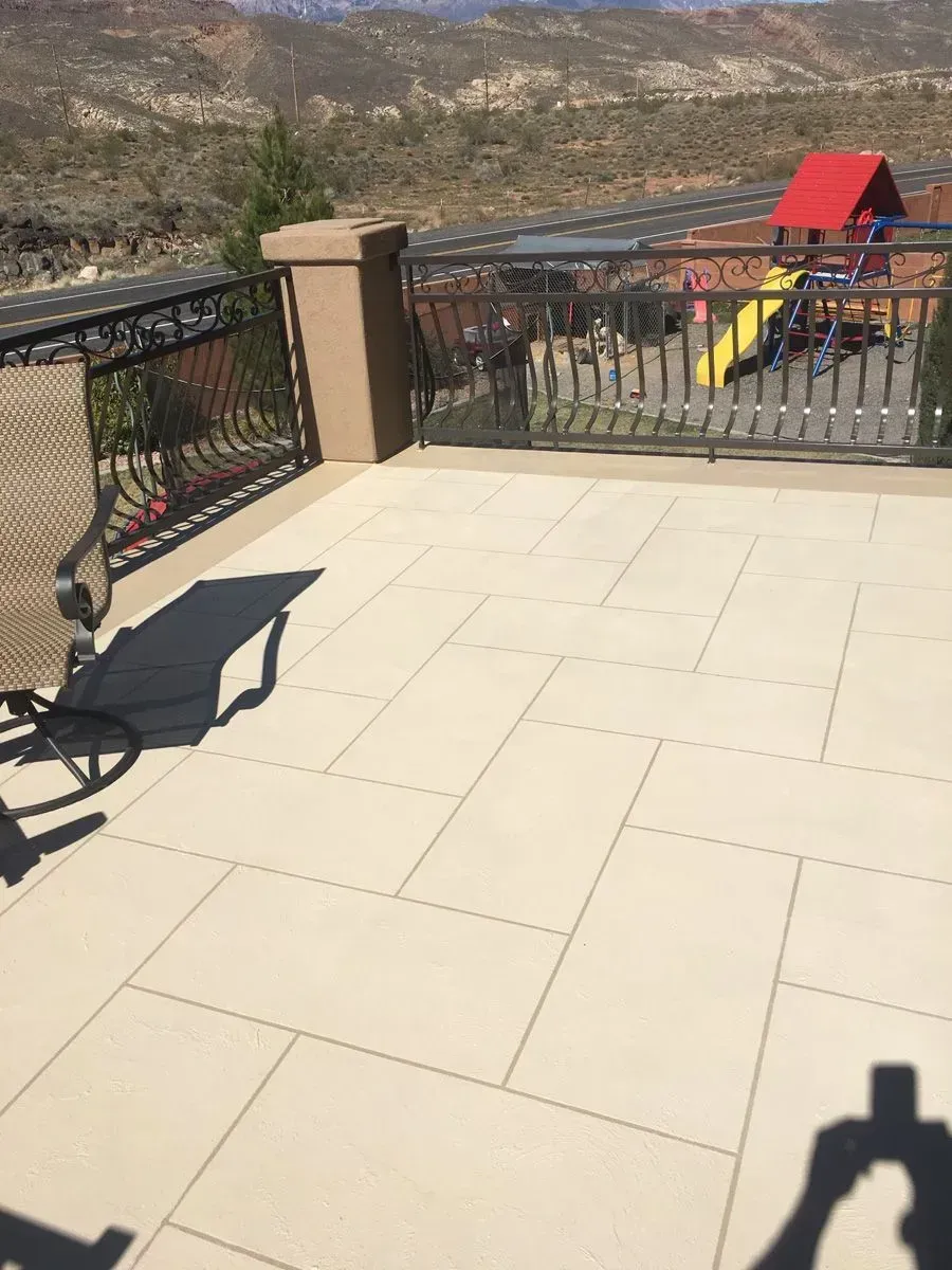 Patio with light-colored tiles, black railing, view of mountains and playground in the distance.