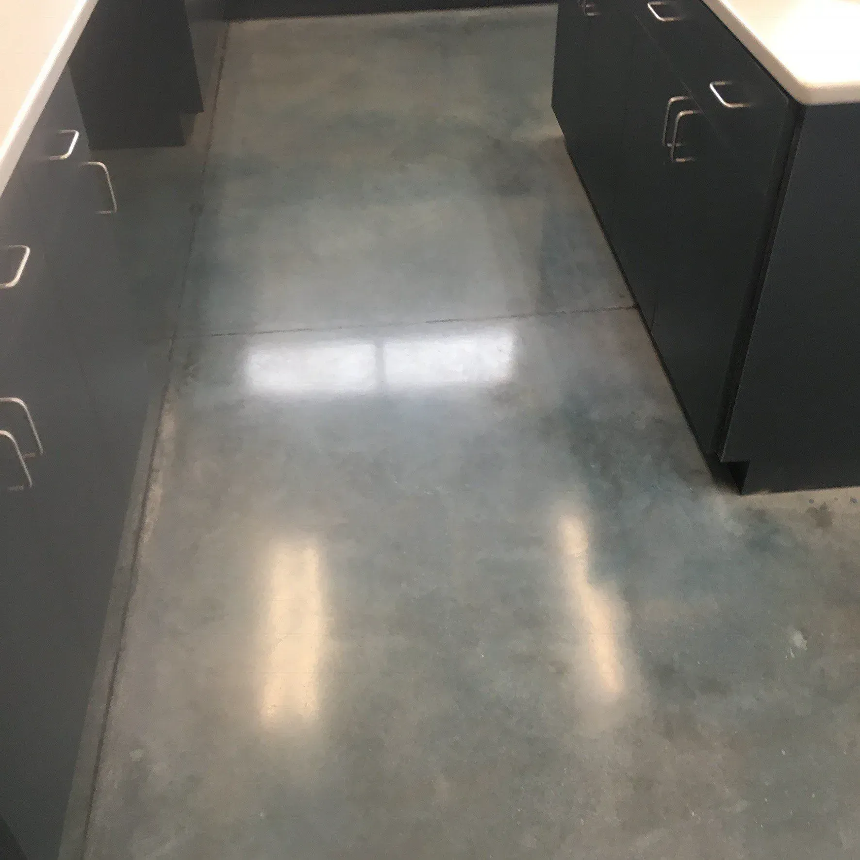 Polished concrete floor between two rows of dark gray cabinets with silver handles.