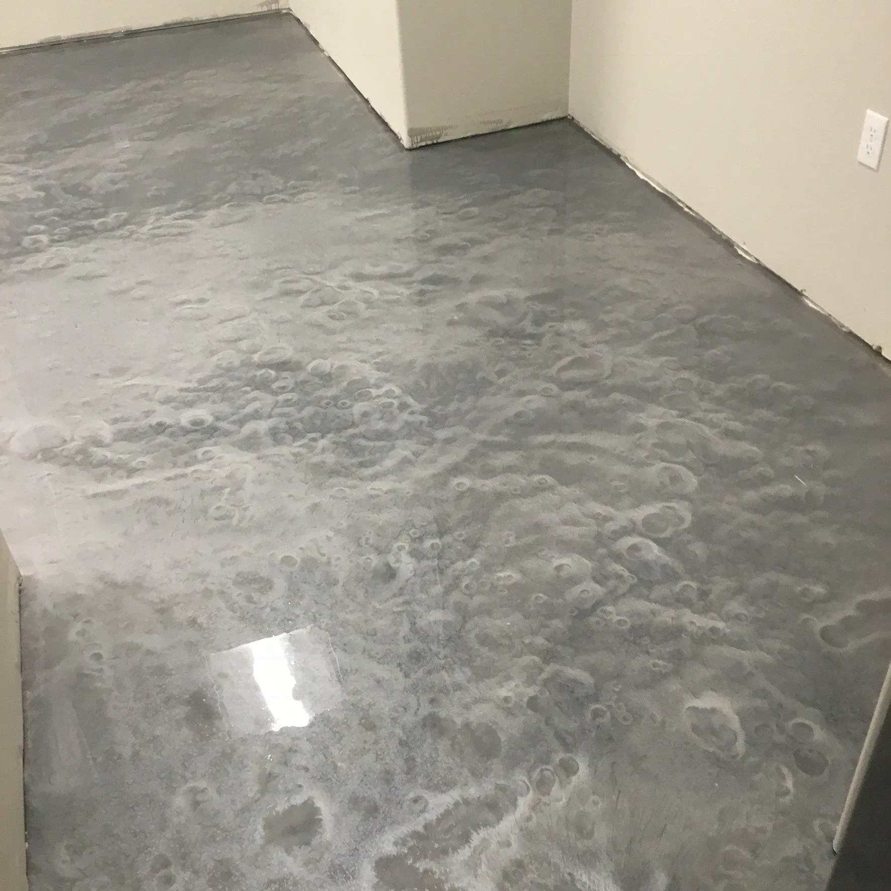 Metallic silver epoxy floor in a room with beige walls and an electrical outlet.