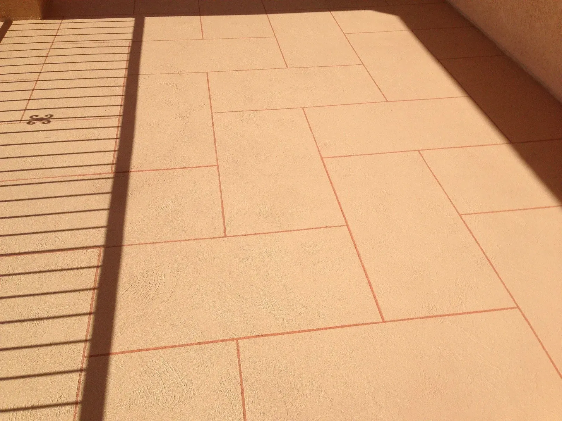Tan rectangular paving stones with red grout lines, in sunlight.