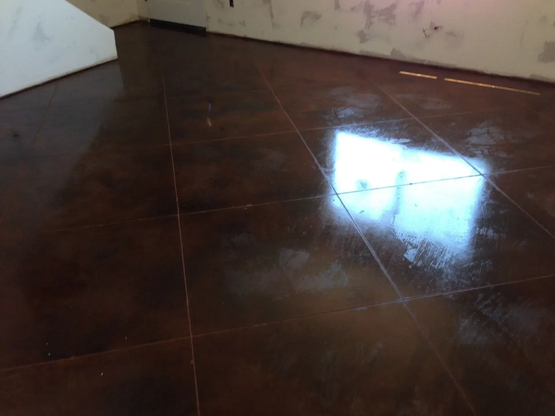 Brown, glossy tiled floor reflecting light in a corner of a room.