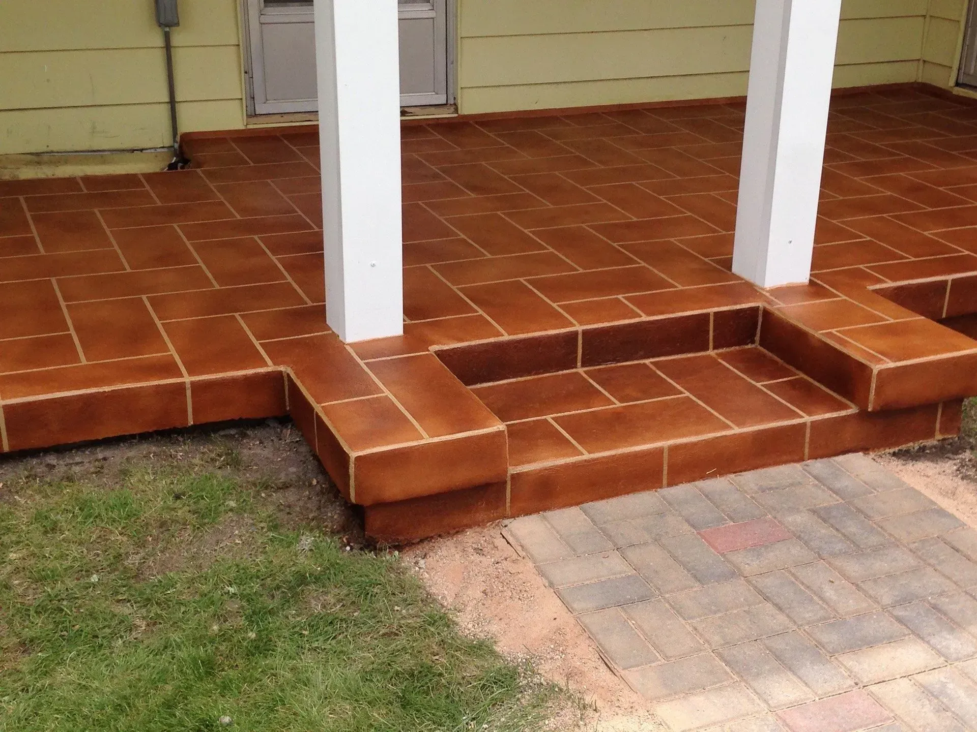 Brown tiled porch with steps, white columns, and brick walkway.