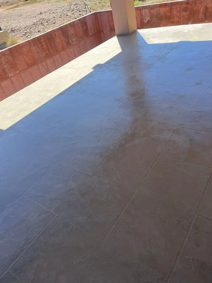 Exterior concrete patio, light brown and gray tones, under partial sunlight, next to reddish wall.